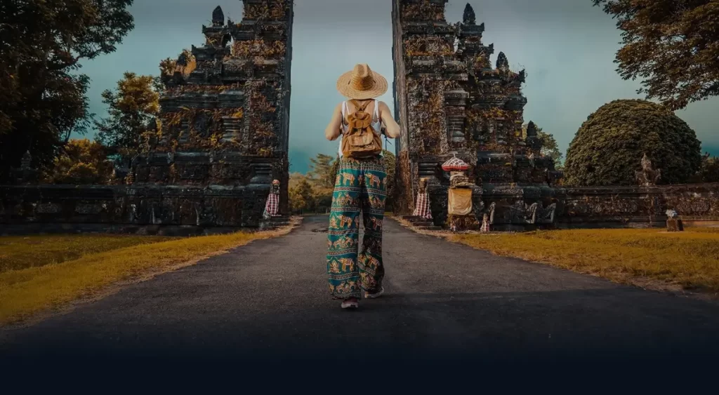 Explore Bali's Enchanting Temples A solo traveler dressed in colorful attire walks towards the towering, intricately carved gates of a Balinese temple, capturing the essence of spiritual and cultural exploration in Bali.